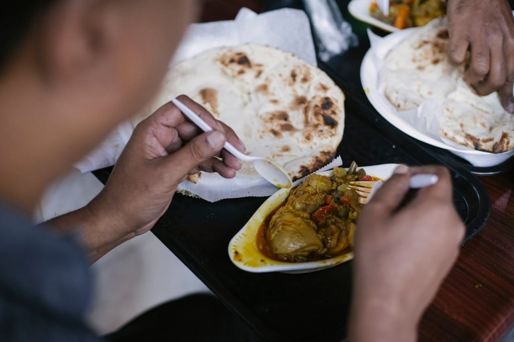 A person enjoying a flavorful curry meal with naan bread, using disposable cutlery at a dining setting.