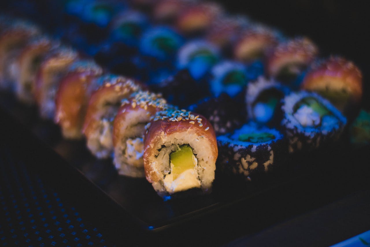 Delicious sushi rolls with avocado and sesame seeds on a dark platter, ideal dinner option.